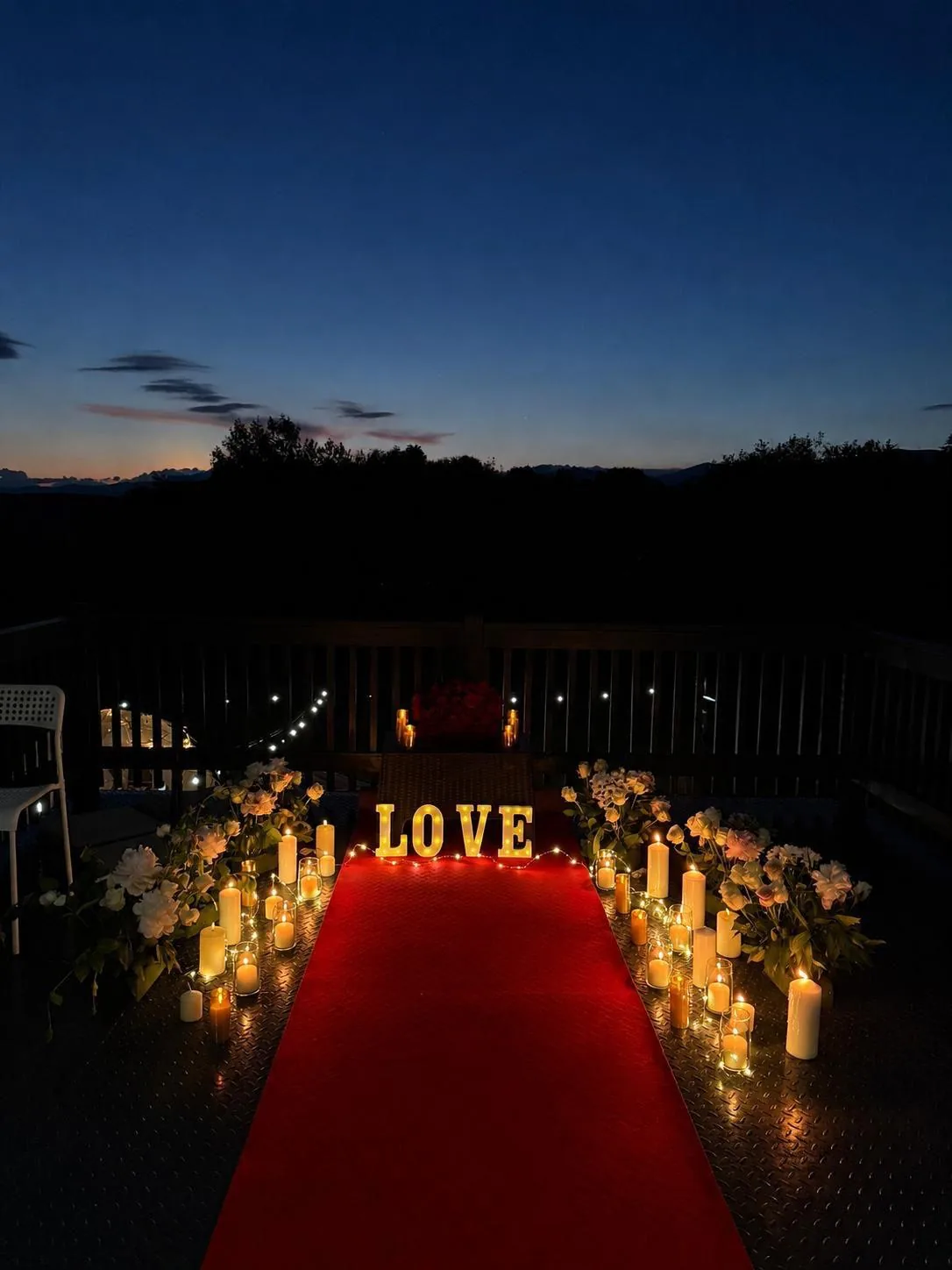 Covor roșu cu litere LOVE luminate și lumânări pe terasă, la asfințit, decor pentru o cerere în căsătorie